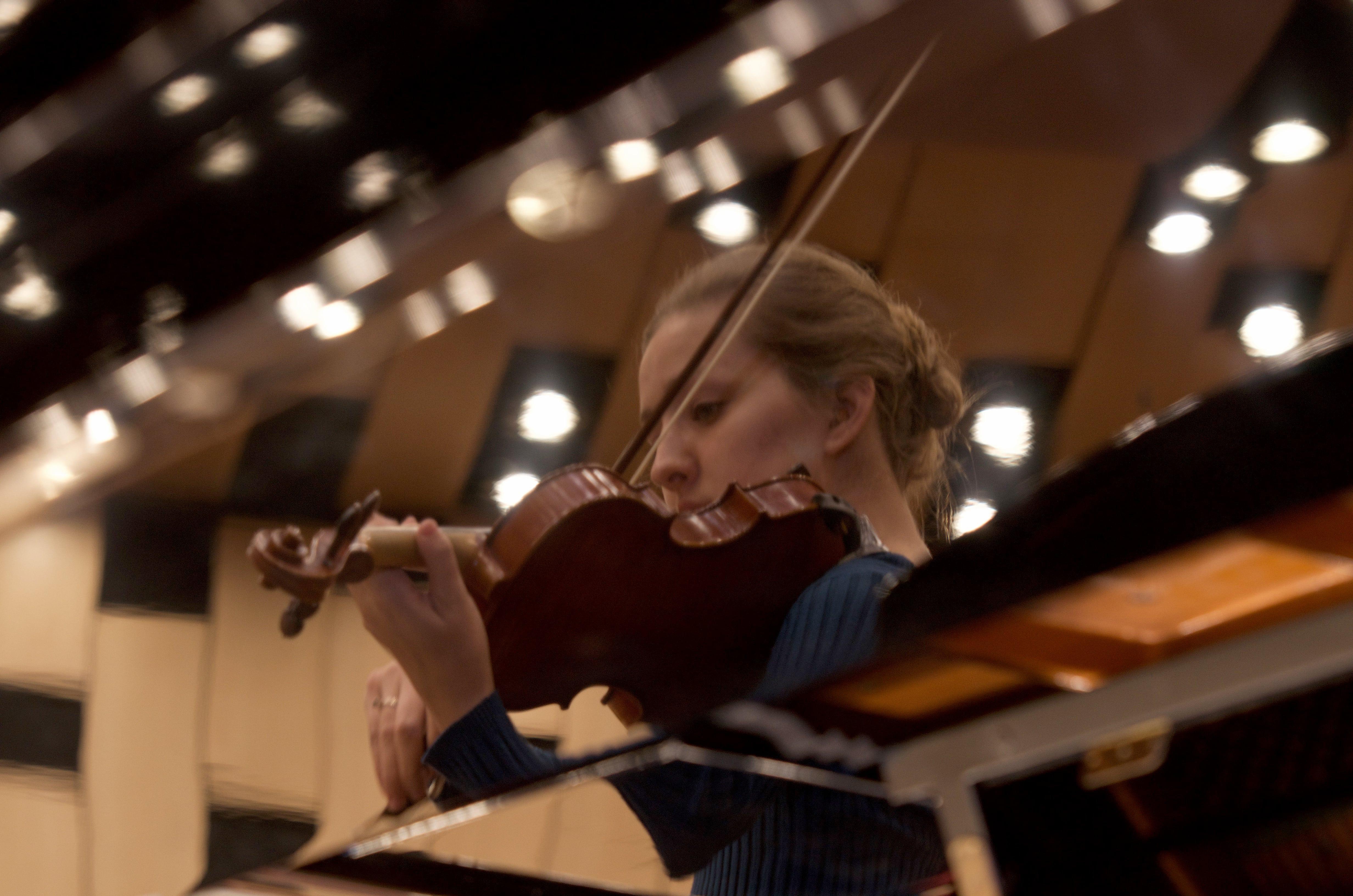 The reflection of a violinist performing, reflected off of the lid of a grand piano.